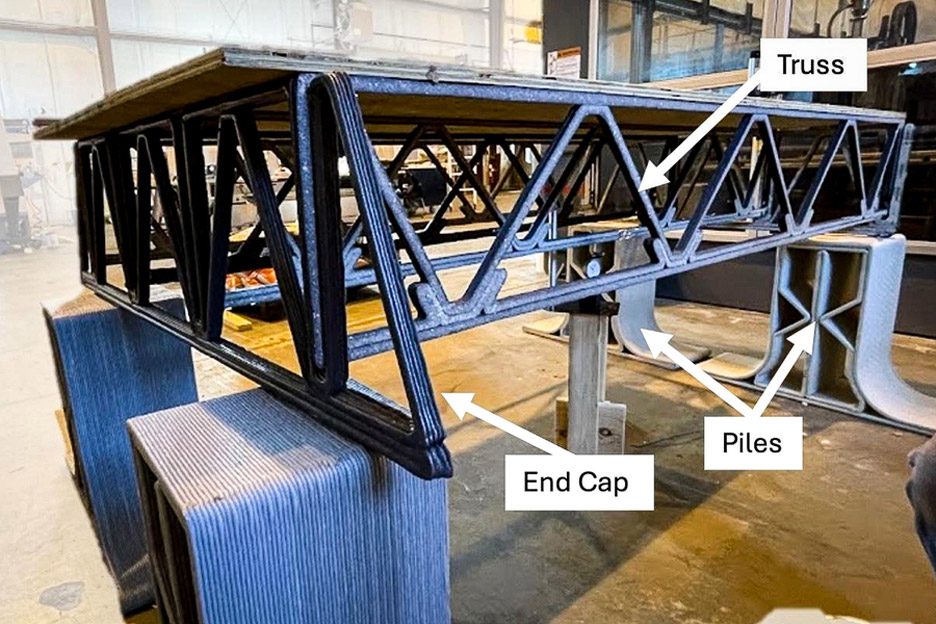 Close-up photo of an experimental floor truss made from plastic-glass composite material with labels pointing out the end cap, truss and piles