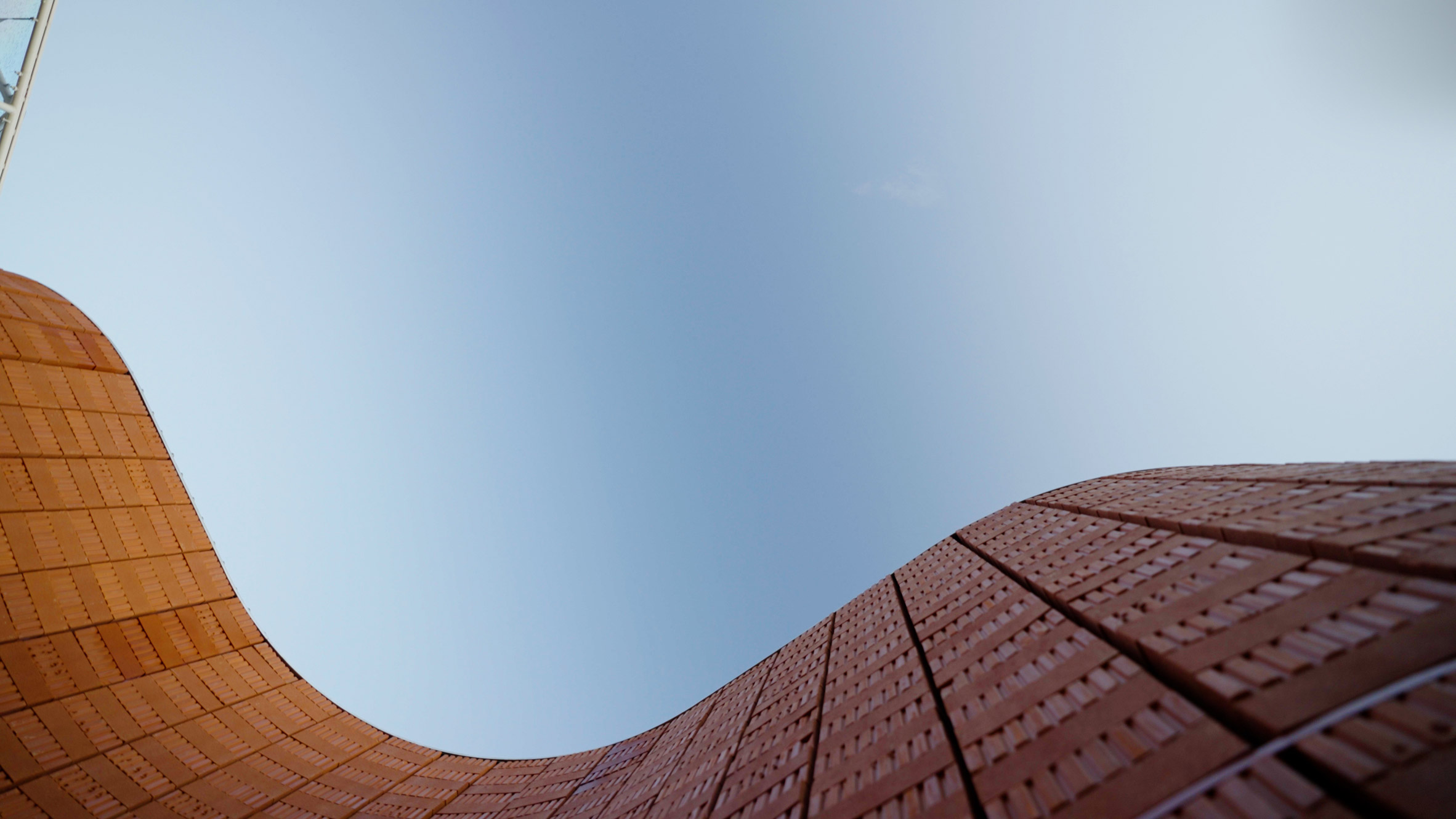 Low-angle view looking upward between two curving red-brick walls that frame a clear blue sky