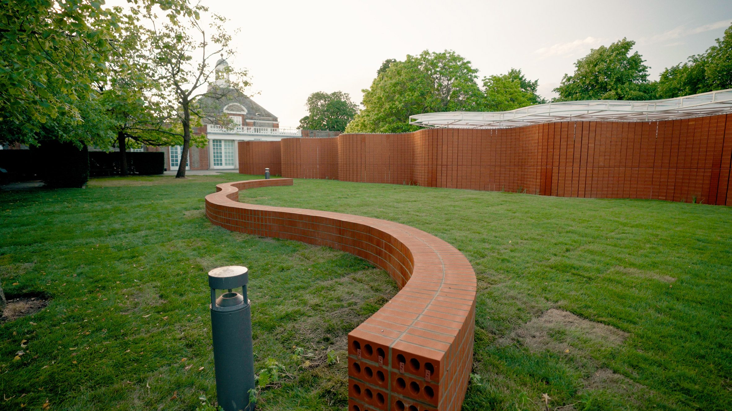 A low winding brick wall in front of the Serpentine Pavilion