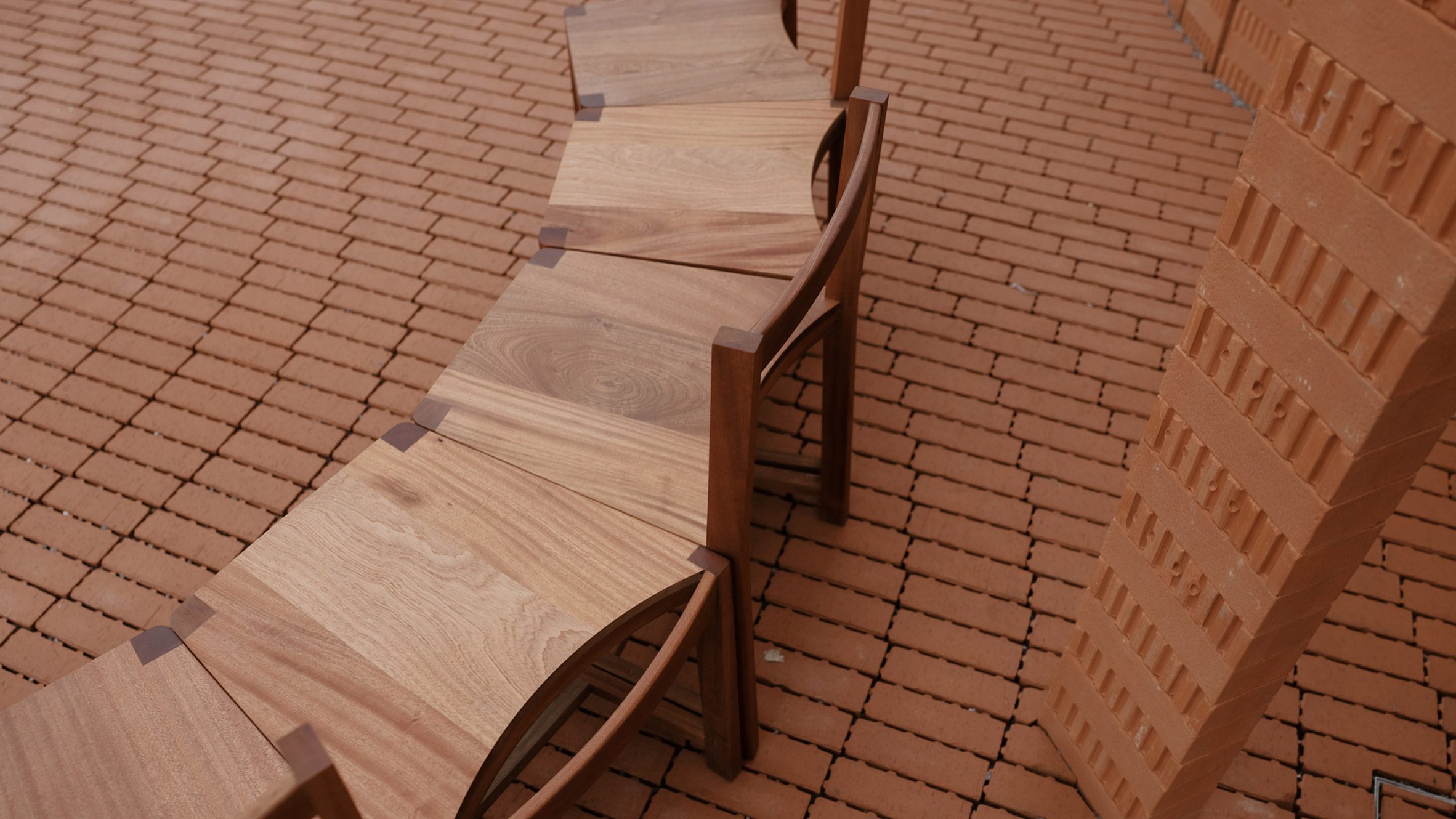 Curved wooden seating arranged on a brick floor beside one of the pavilion's red-brick walls
