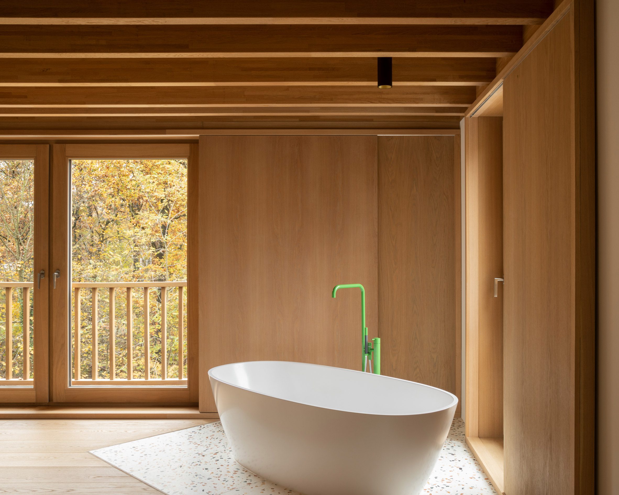 White freestanding bath with a green tap in a timber-clad room